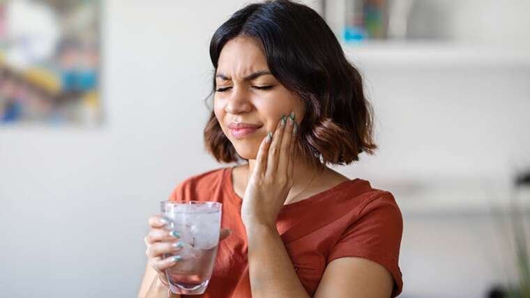 Woman experiencing sensitive teeth after drinking a glass of cold water.